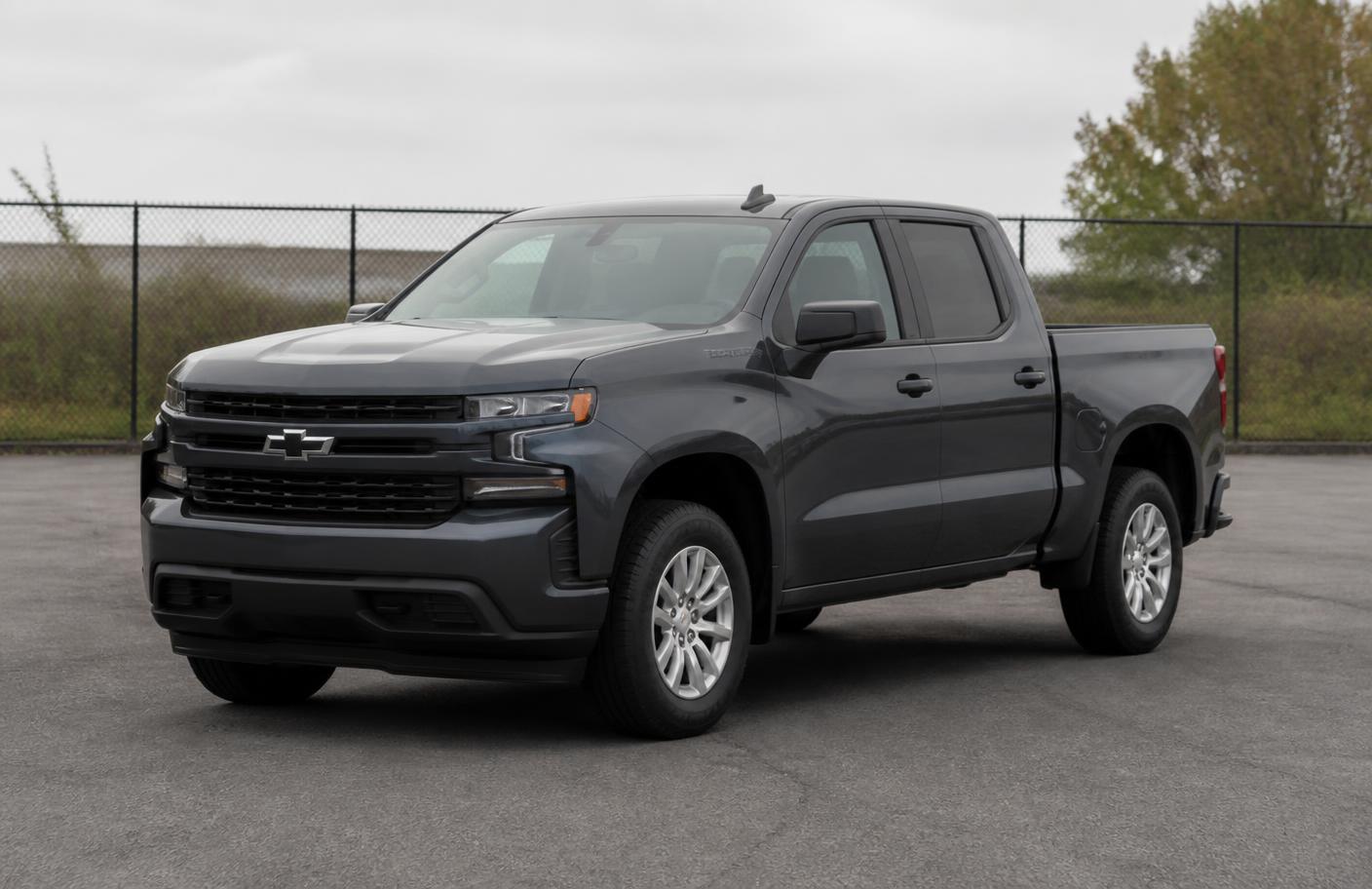 A dark gray pickup truck parked on a plain concrete lot under overcast light